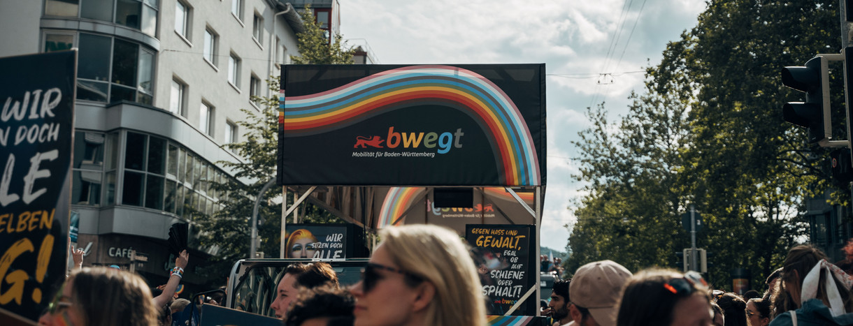 buntes Regenbogen-Logo von bwegt über einer Menschenmasse mit ebenfalls bunten Plakaten