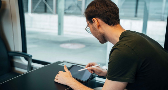 Mann arbeitet am Tablet in einem Zug.