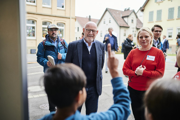 Verkehrssicherheit MOVERS – Aktiv zur Schule Minister Hermann lächelnd vor einer Gruppe von Kindern, ein Junge meldet sich.