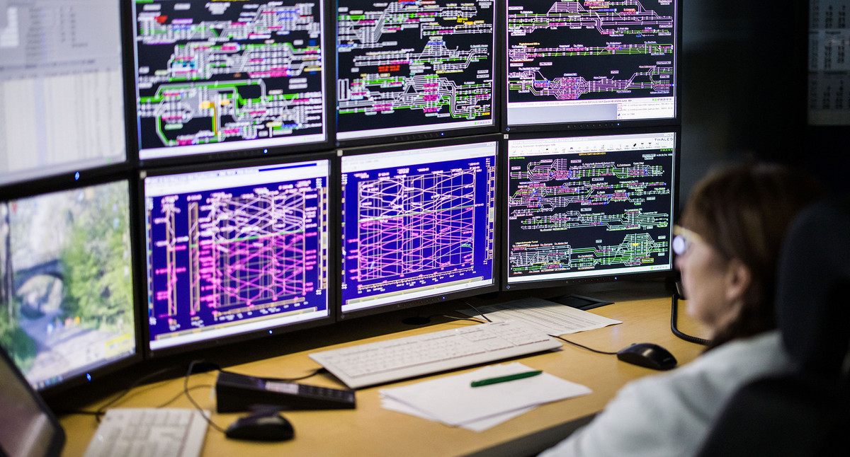 Schreibtisch mit unzähligen Monitoren auf denen ein Schienennetz dargestellt ist.