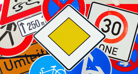 Mehrere Verkehrsschilder liegen übereinander. Darunter ein Vorfahrtsschild und ein Zone 30-Schild