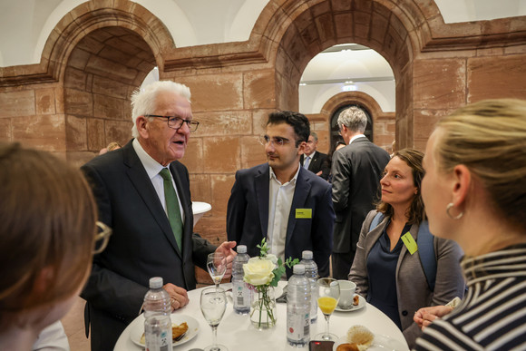 Zusammenhalt in der Transformation Tagung „Gemeinsam handeln“ Ministerpräsident Winfried Kretschmann (zweiter von links) an einem Stehtisch im Gespräch mit Gästen.