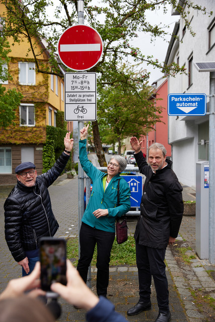 Drei Personen zeigen auf ein Verkehrsschild das anzeigt, dass eine Durchffahrt zu bestimmten Uhrzeiten verboten ist.