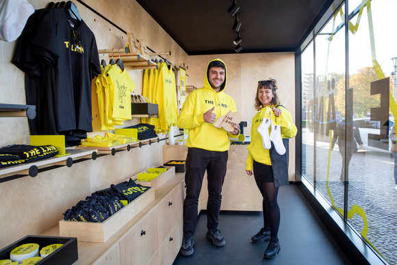 Imagekampagne Baden-Württemberg ist „THE LÄND“ Ein Mann und eine Frau im mobilen „Fän“-Shop in Form eines umgebauten Frachtcontainers vor dem Neuen Schloss in Stuttgart