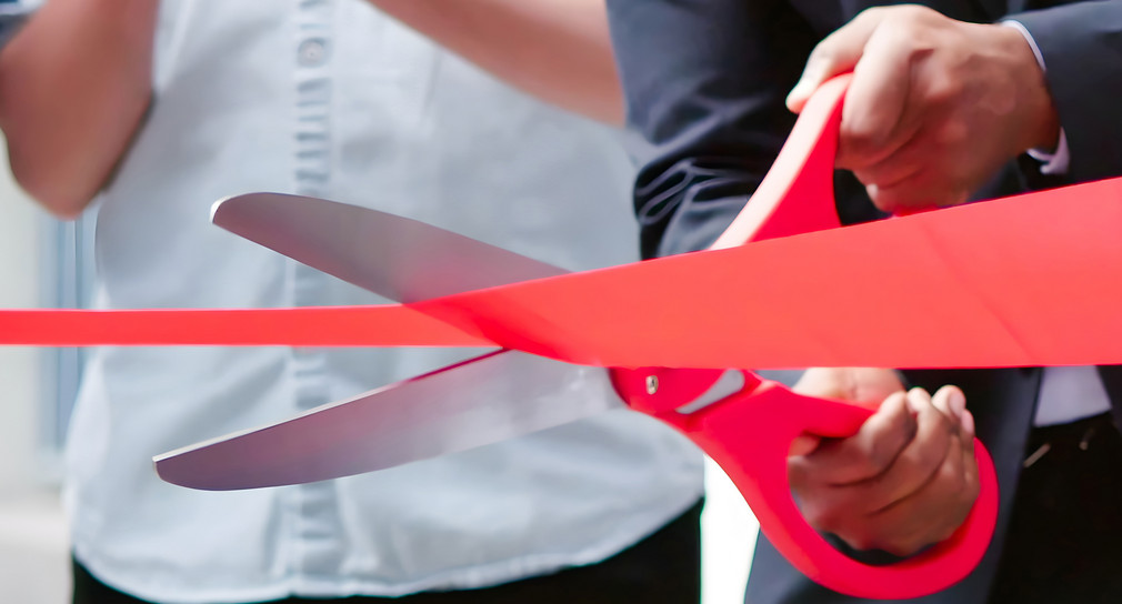 Eine Person schneidet mit einer großen Schere ein Band zur Eröffnung durch. 