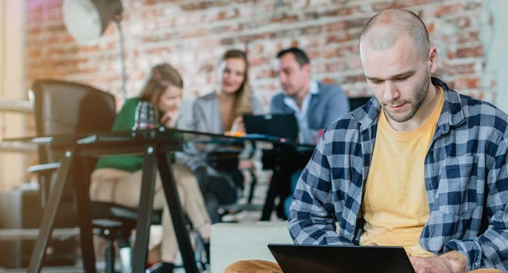 Mann sitzt mit Laptop auf dem Schoß auf dem Boden und arbeitet.