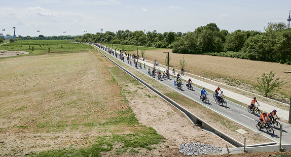 Eine große Kolonne von Fahrradfahrerinnen und -fahrern radeln auf einem neuem Radweg. Die Personen tragen alle einen Helm. 