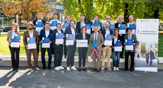 Vertreterinnen und Vertreter der Kommunen halten ihre Urkunde hoch, mit Staatssekretär Rainmund Haser.