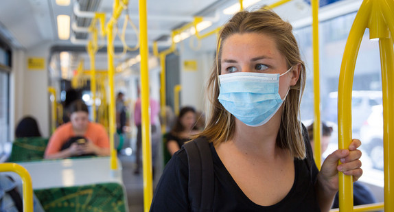 Schülerin mit aufgesetzter Maske steht in einem Bus und hält sich fest.