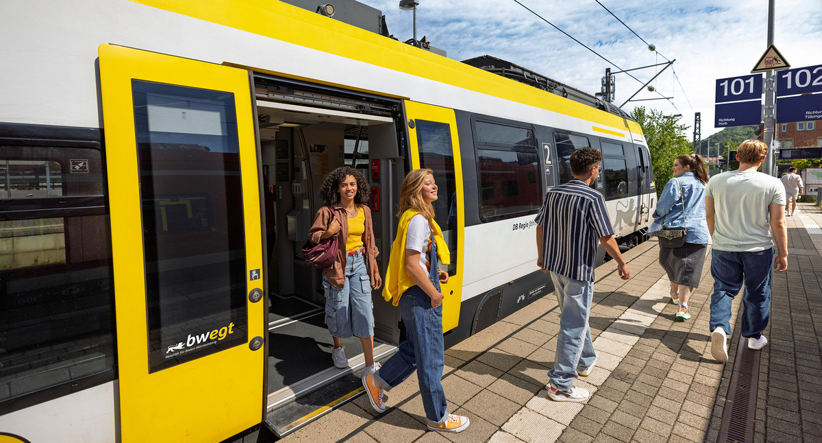 Junge Menschen steigen aus einem Zug am Bahnsteig aus.