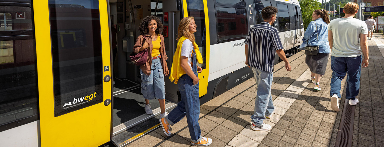 Junge Menschen steigen aus einem Zug am Bahnsteig aus.