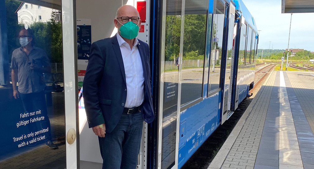 Verkehrsminister Hermann steht an der offenen Türe eines blauen Zuges, der an einem Bahnsteig steht.