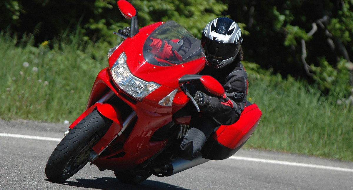 Ein Motorradfahrer lehnt sich mit seinem roten Motorrad in eine Kurve.