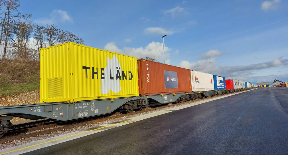 Container, unter anderem einer im THE-LÄND-Design, auf einem Güterzug.
