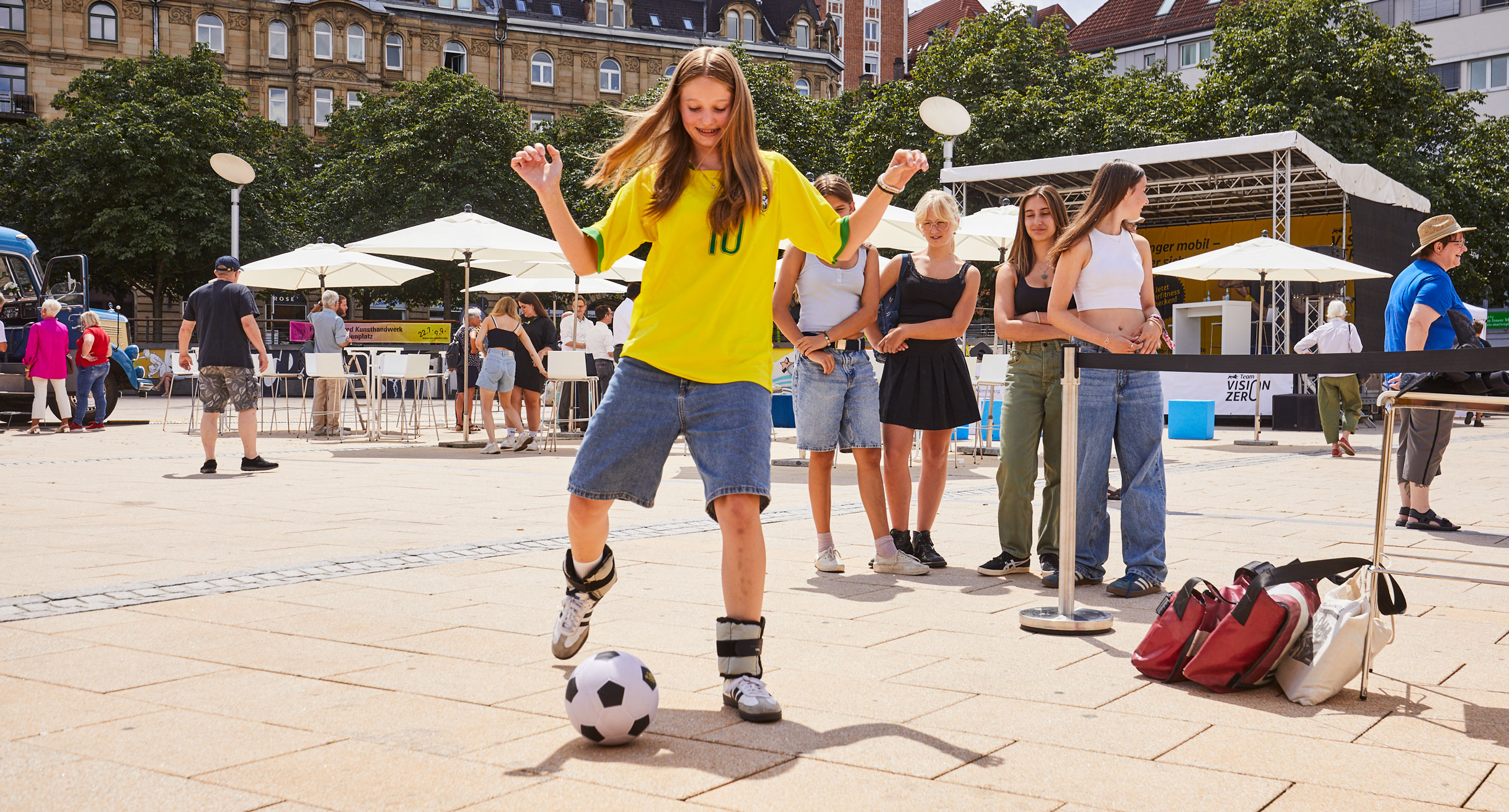 Mädchen mit gelbem T-Shirt spielt Fußball mit Gewichten an den Füßen.