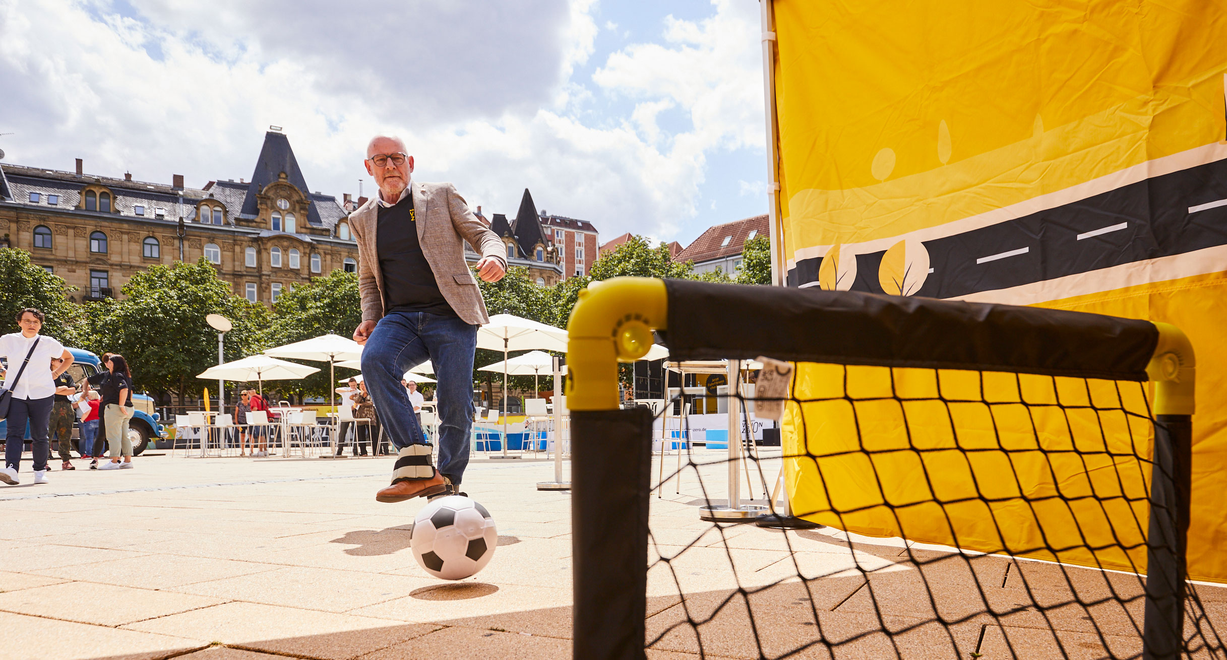 Verkehrsminister Winfried Hermann spielt Fußball mit Gewichten an den Füßen.