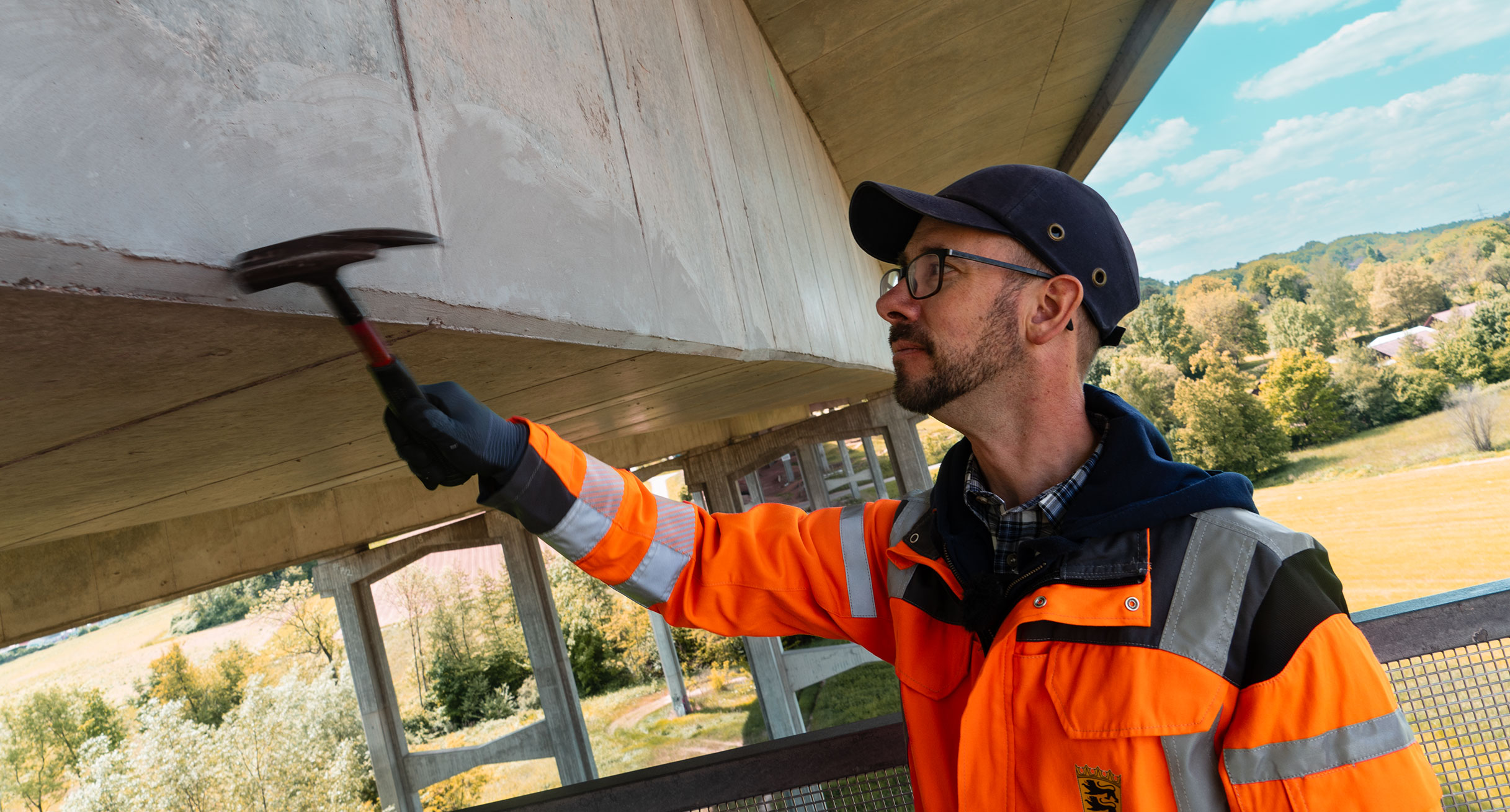 An Mann in Warnweste klopft mit dem Hammer an einem Brückenpfeiler.