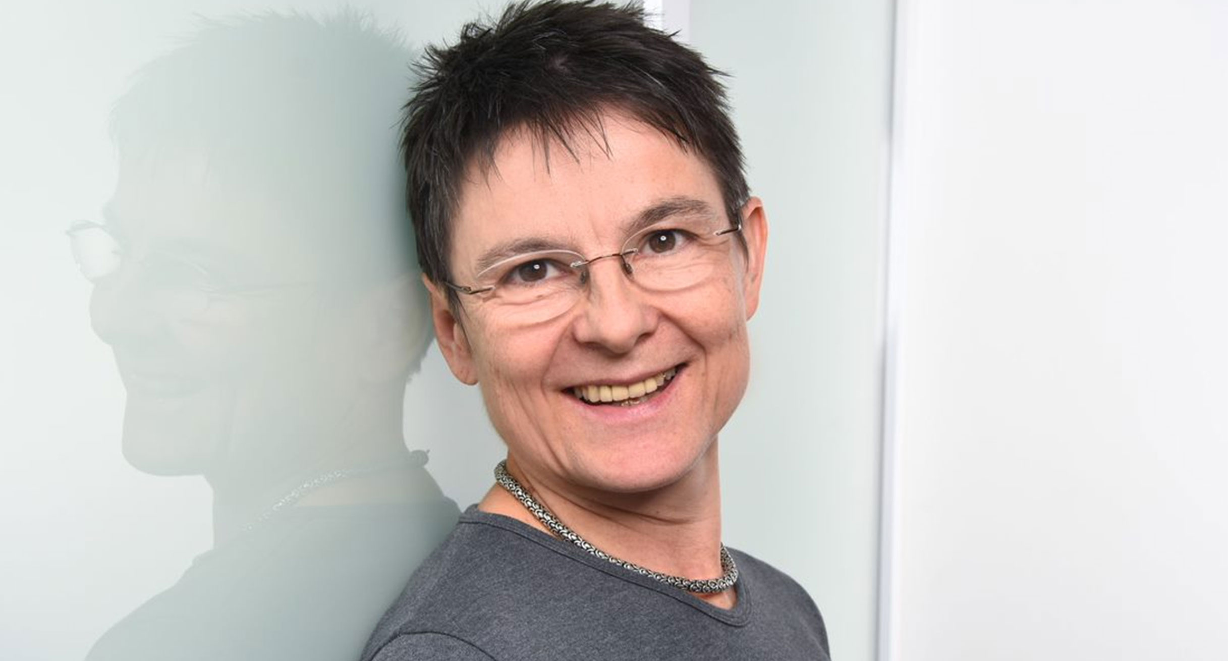 Porträtfoto einer mittel-alten Frau sie an einer Wand lehnt.